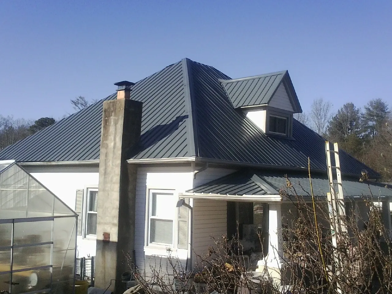 Dark blue standing seam metal roof on a white farmhouse with dormer — Slate & Tile Roof Repair by Roofing Brothers in Lonepine