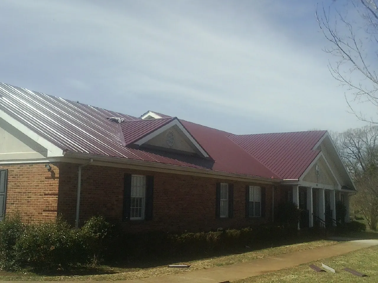 Red metal roof with gabled entries on a long brick building, from a Hail Damage Roof Repair job in Lonepine
