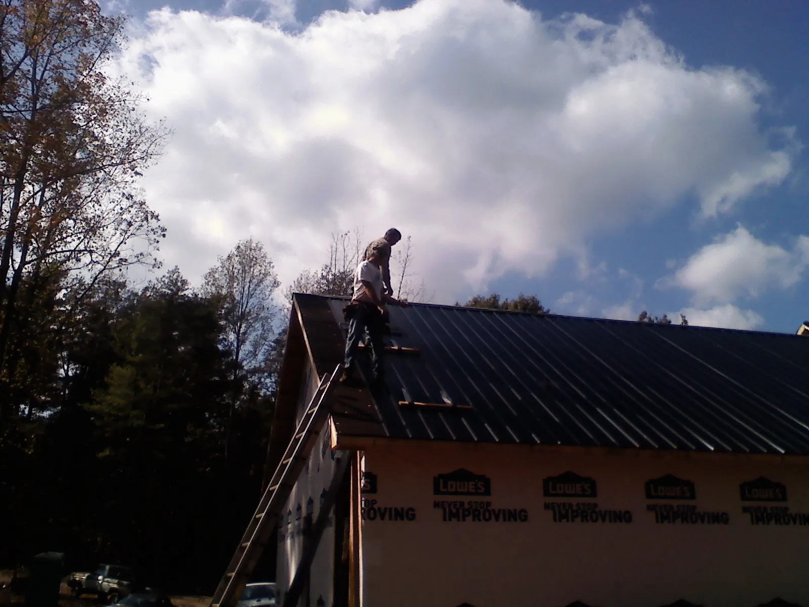 Roofer fastening dark metal panels high against a cloudy sky, from a Roof Inspection job in Lonepine